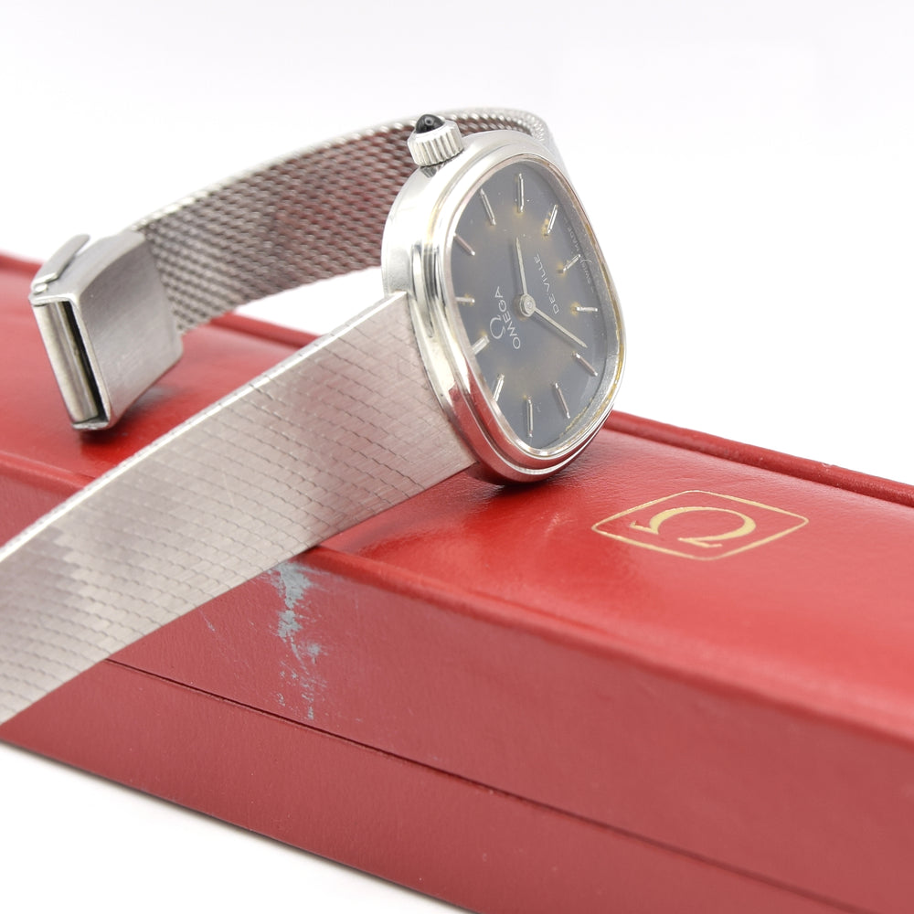 Omega wristwatch with a silver-tone mesh strap and silver-tone case, resting on a red Omega presentation box against a white background.