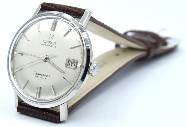 An Omega Swamaster automatic wristwatch with a silver-toned case, cream-colored dial, and a brown leather strap, photographed on a clean white background.